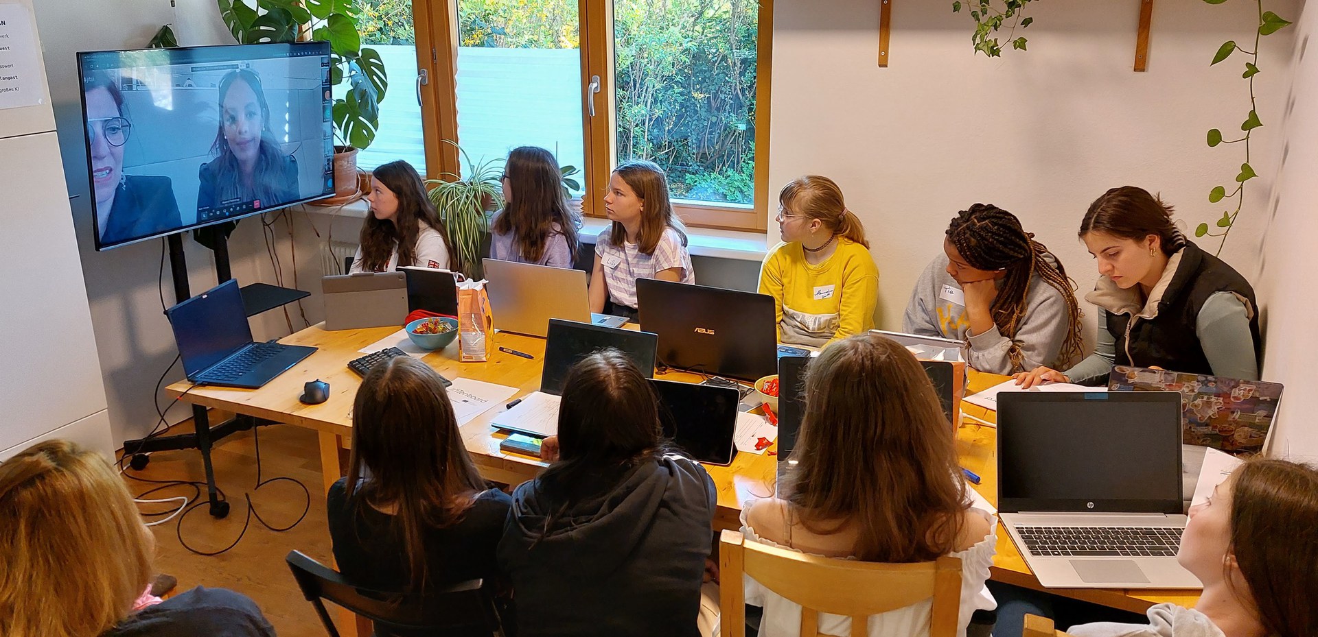 10 girls around a conference table watching an interview on a large screen.
